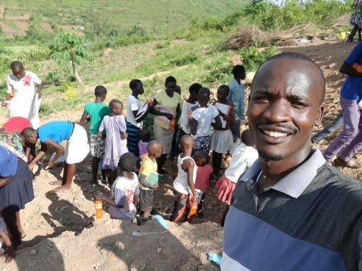 An outdoor selfie with a group of adults and children in the background.