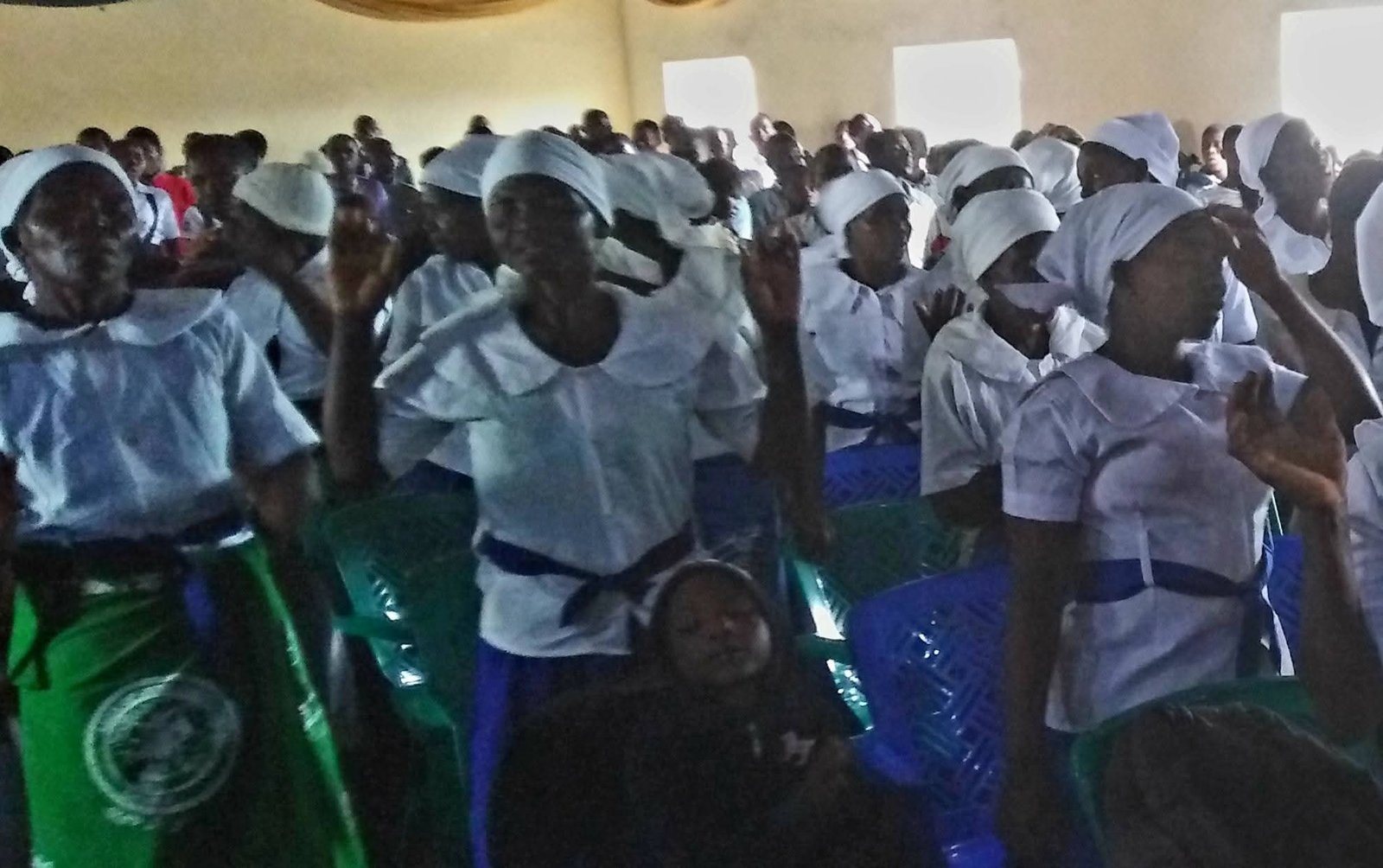 Women in blue and white clothing take part in an indoor church gathering.