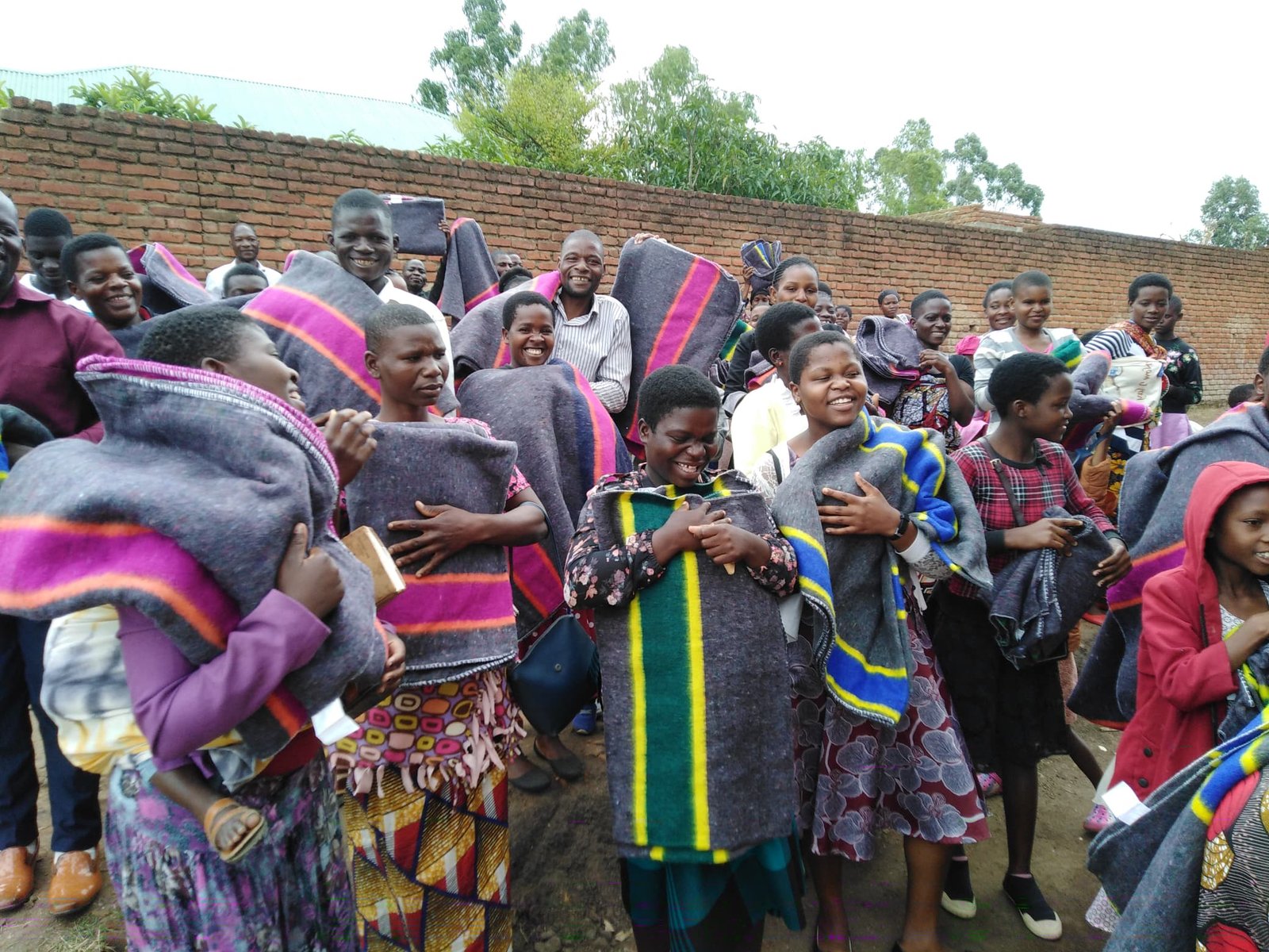Members of an outdoor group hold striped blankets beside a brick wall.