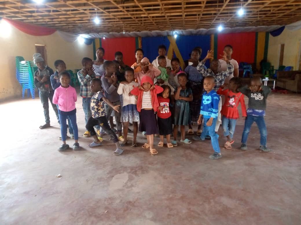Children gather at the front of a church hall, with adults behind them.
