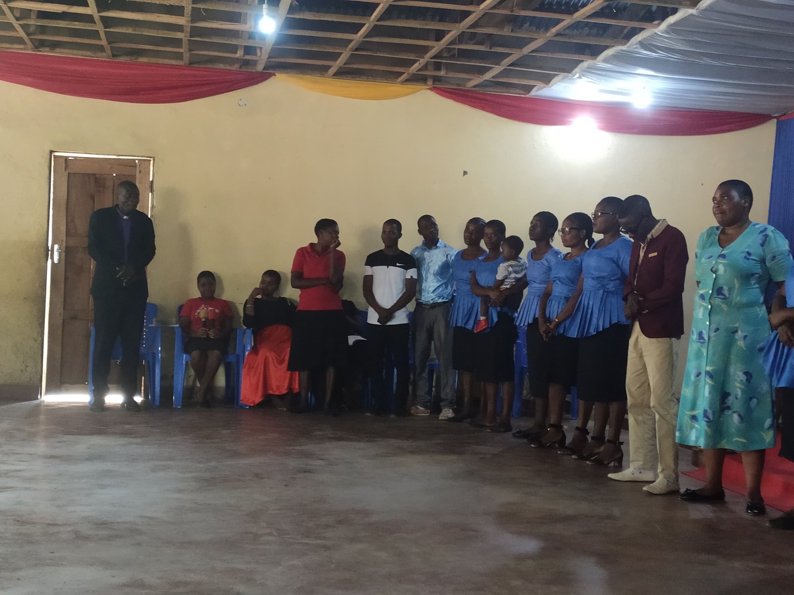 Children and adults form a line along the front wall of a church hall.