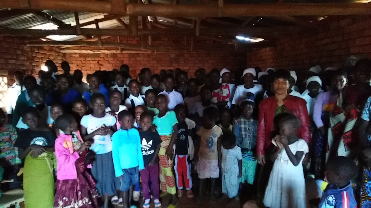 Children and adults gather inside a brick-walled meeting room.