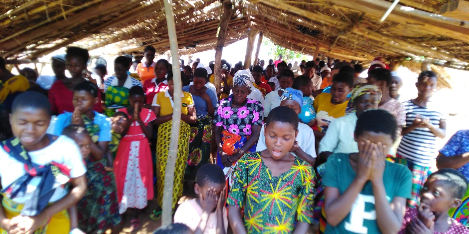 A view of the congregation inside an open-sided thatched shelter.