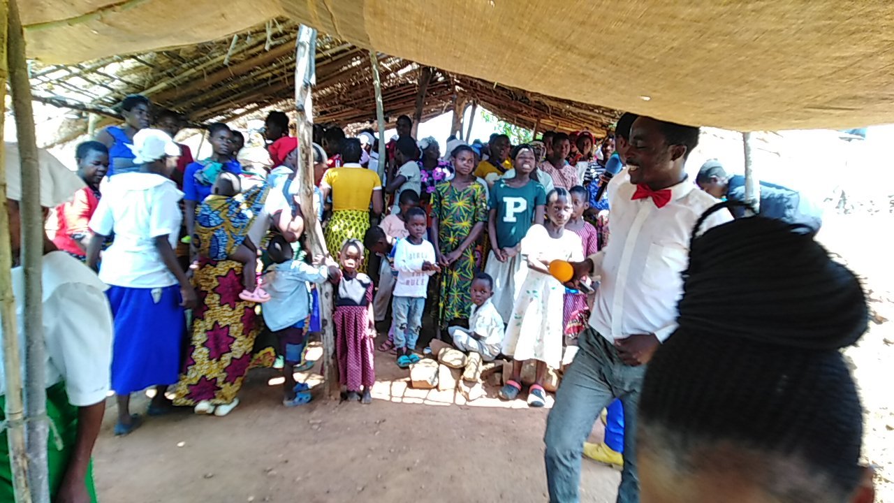 Women and children gather beneath a thatched roof.