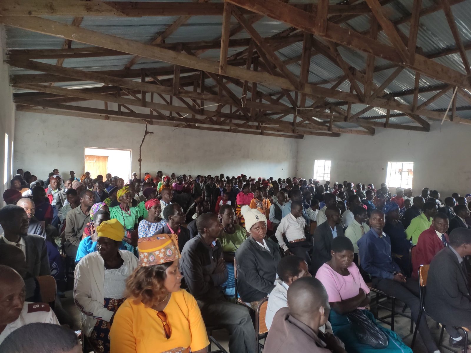 A congregation seated inside a large hall with exposed timber roof framing.