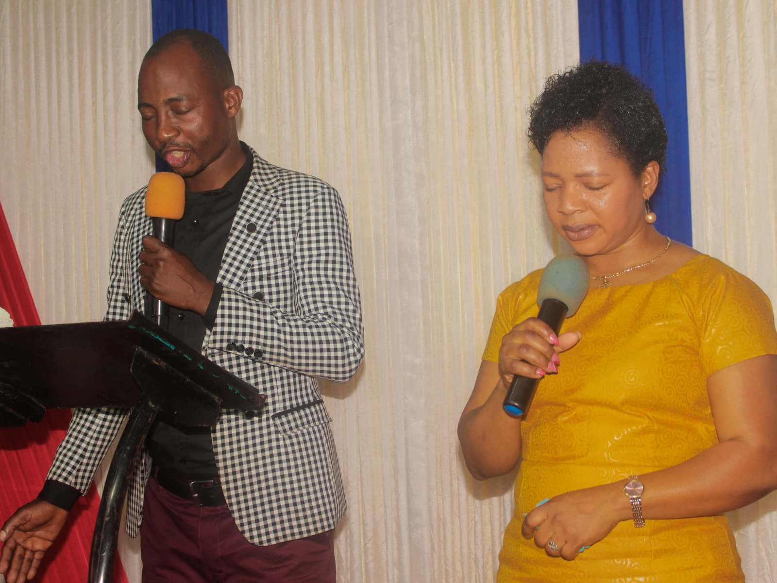 A man and a woman hold microphones beside a lectern.