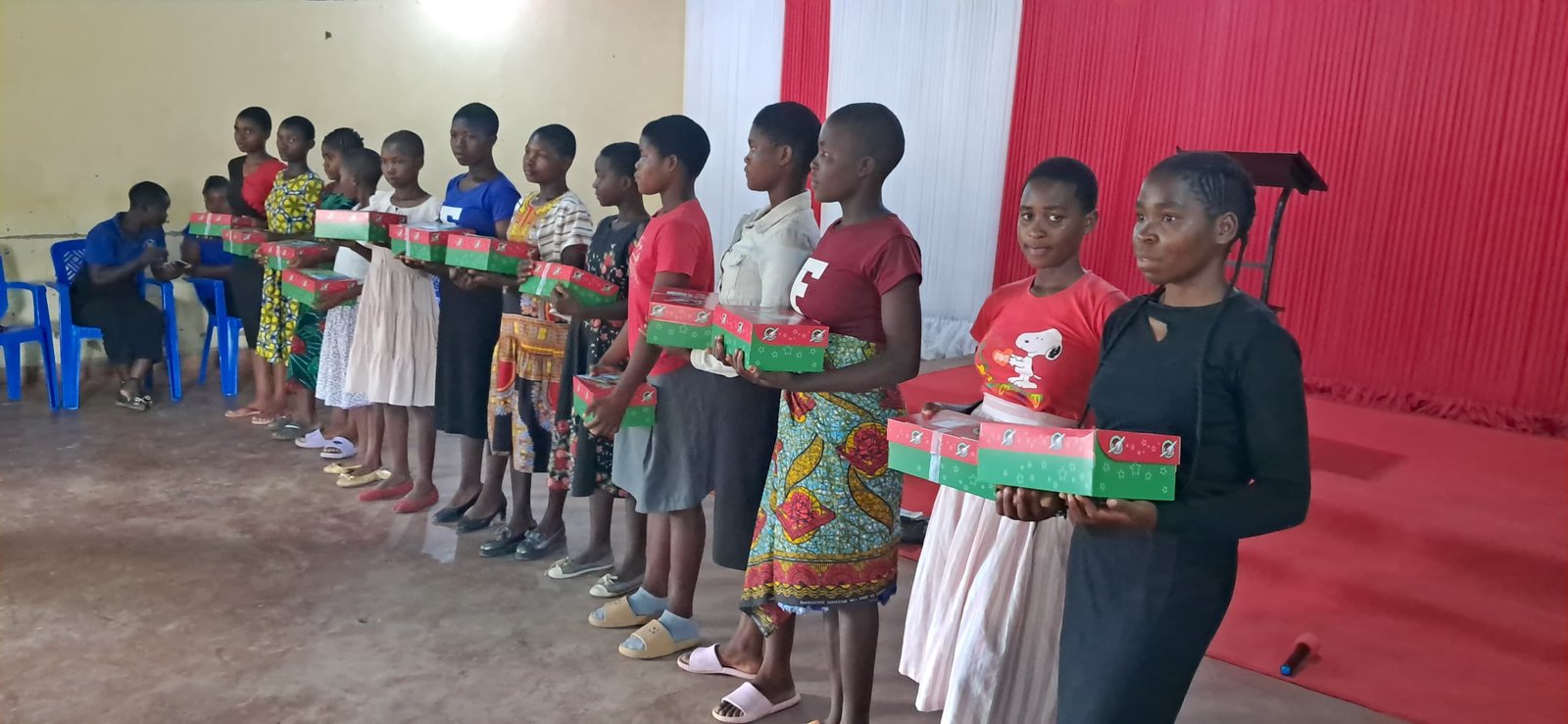 Older children stand in a line holding red and green boxes.