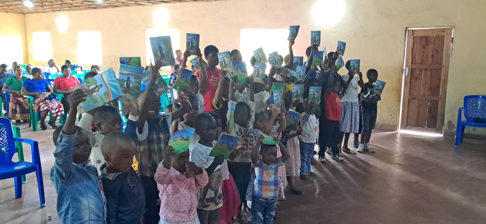 Children hold up printed materials inside a church hall.