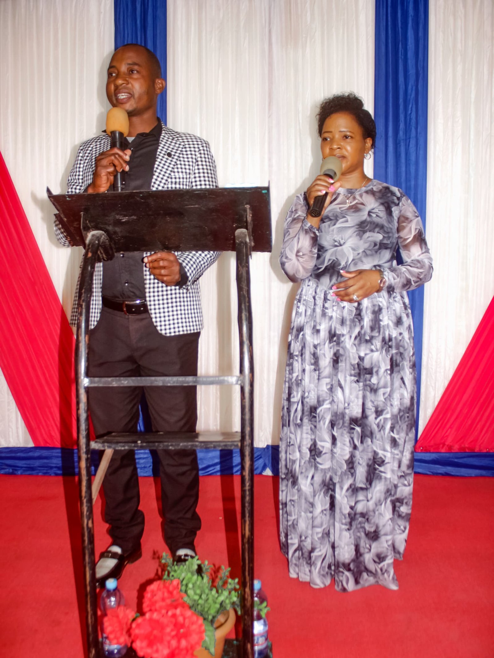 A man and a woman speak with microphones at a lectern.