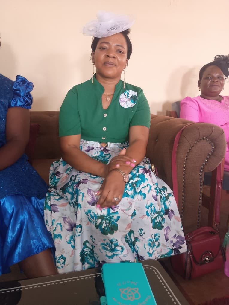 A woman in a green blouse sits indoors, with other women beside her.